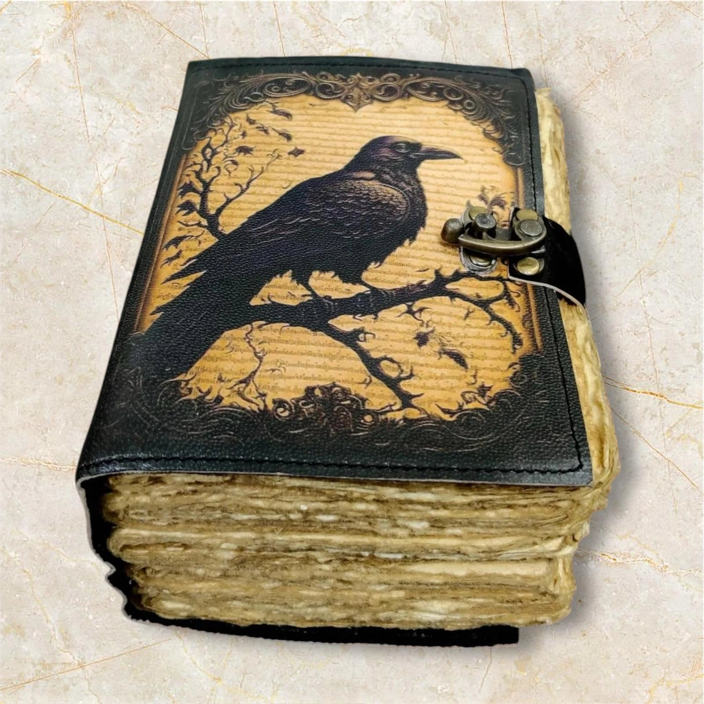 A leather journal on a marbled surface. The cover depicts a drawing of a black crow perched on dark branches.