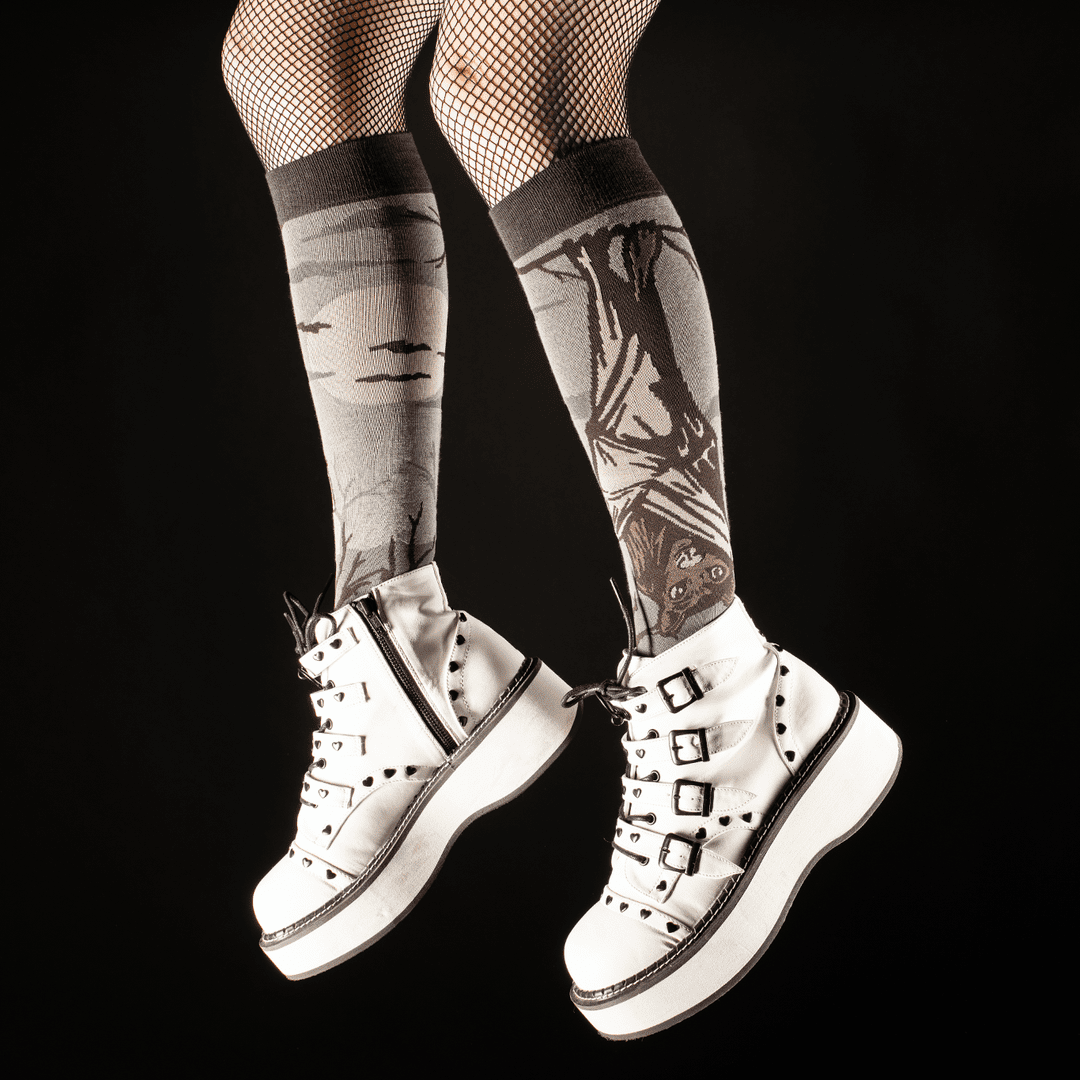 White sneakers with black accents worn with patterned knee-high socks on a black background
