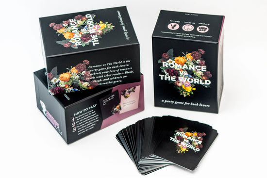 Black boxes on a white background. On the box covers are bouquets of flowers, with white text in the center saying "romance vs the world." A stack of black cards sits in front of the boxes.