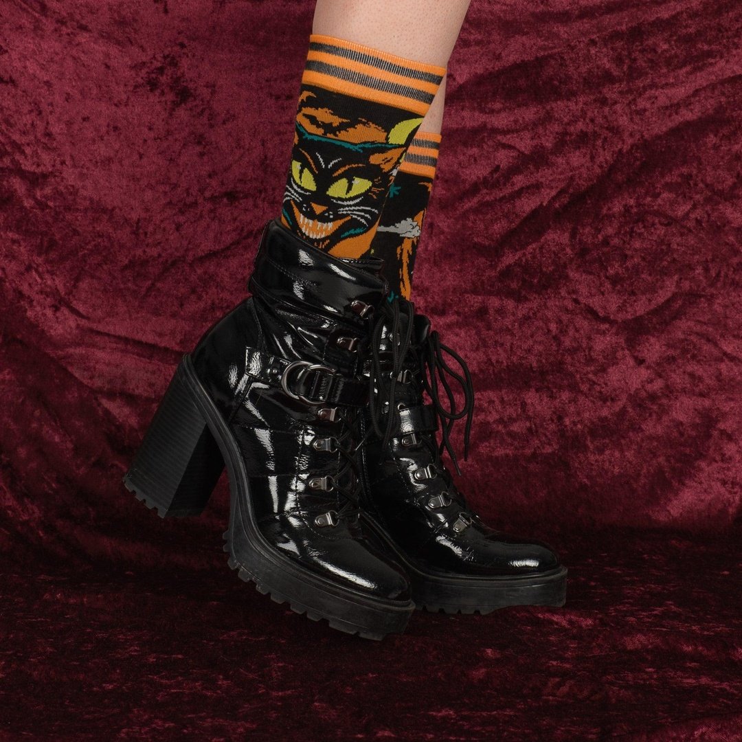 Black high-heeled boots worn with colorful striped socks on a maroon fabric background
