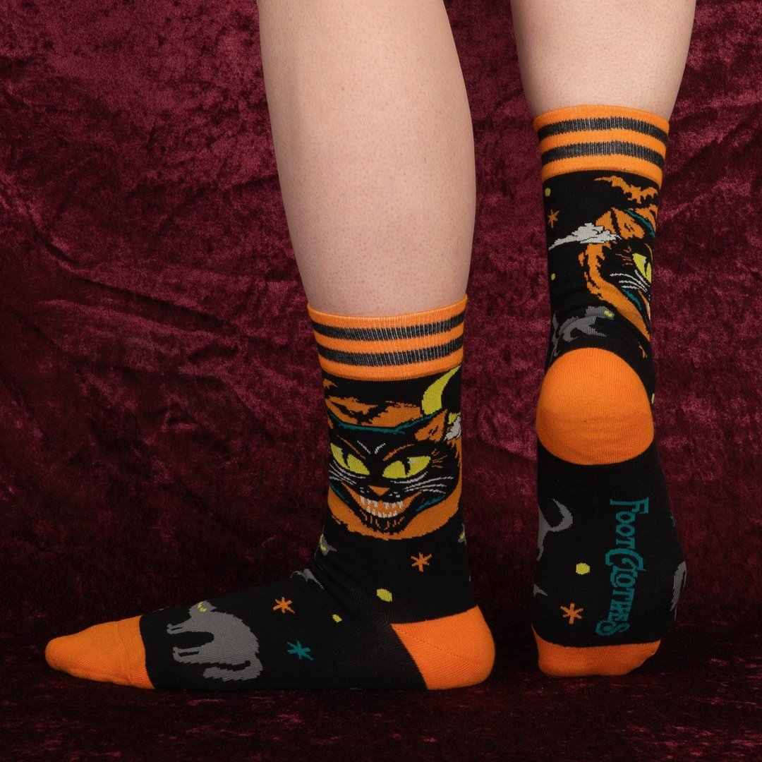 Halloween-themed socks with cat and ghost designs on a maroon background