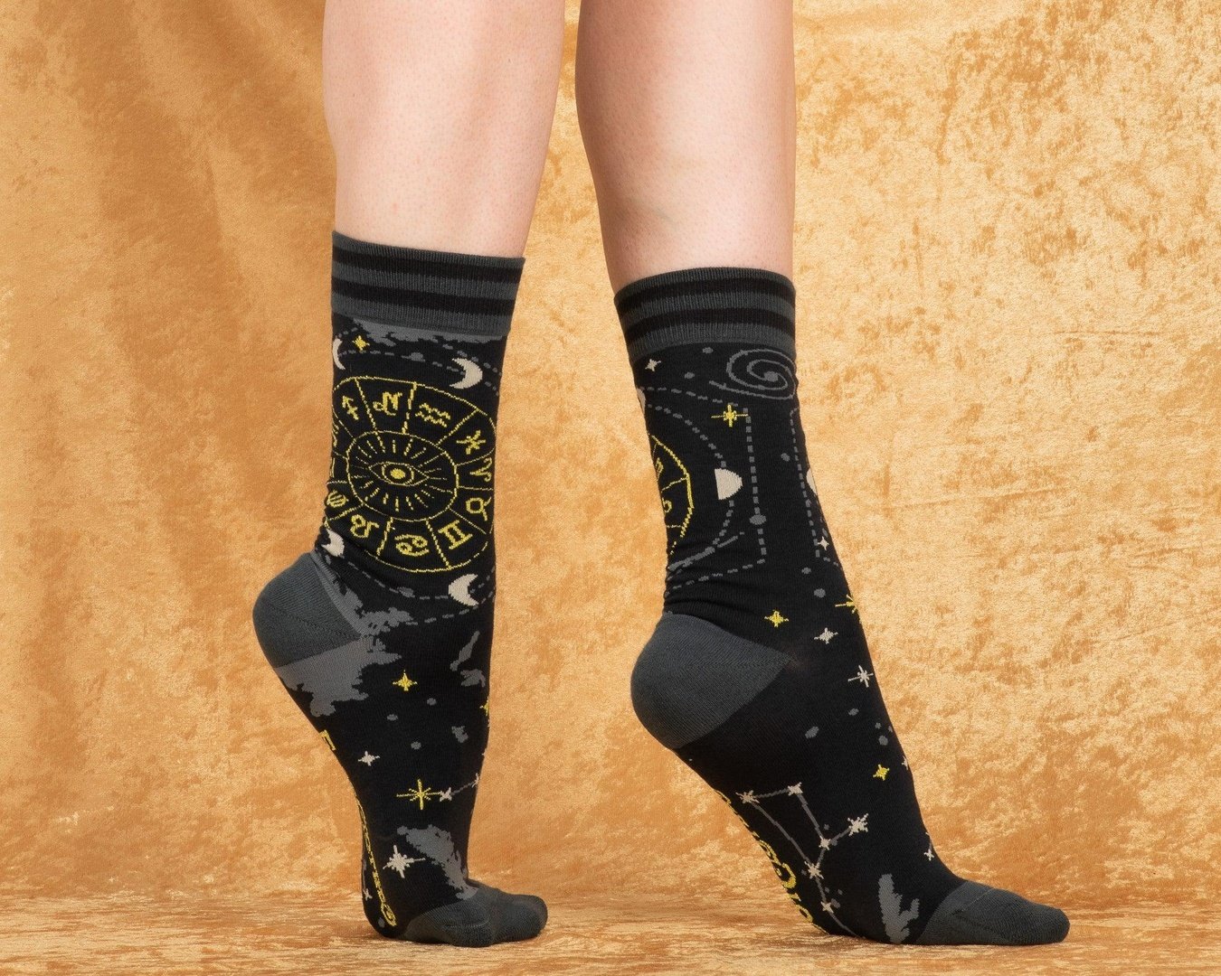 Black socks with star and moon patterns worn by a person on a beige background