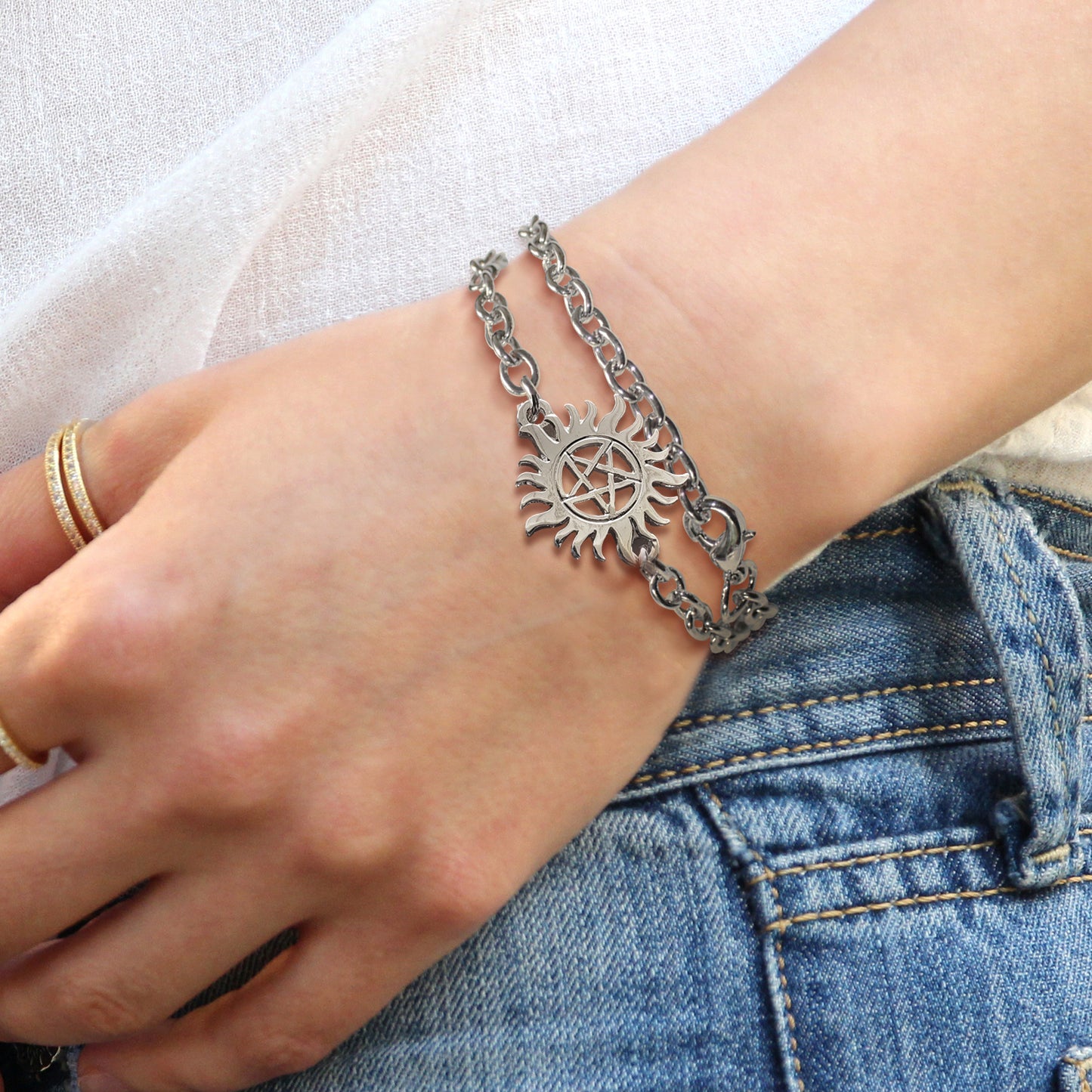 Close up of a model's wrist, wearing a silver bracelet. Attached to the bracelet is a charm in the shape of the anti-possession symbol.