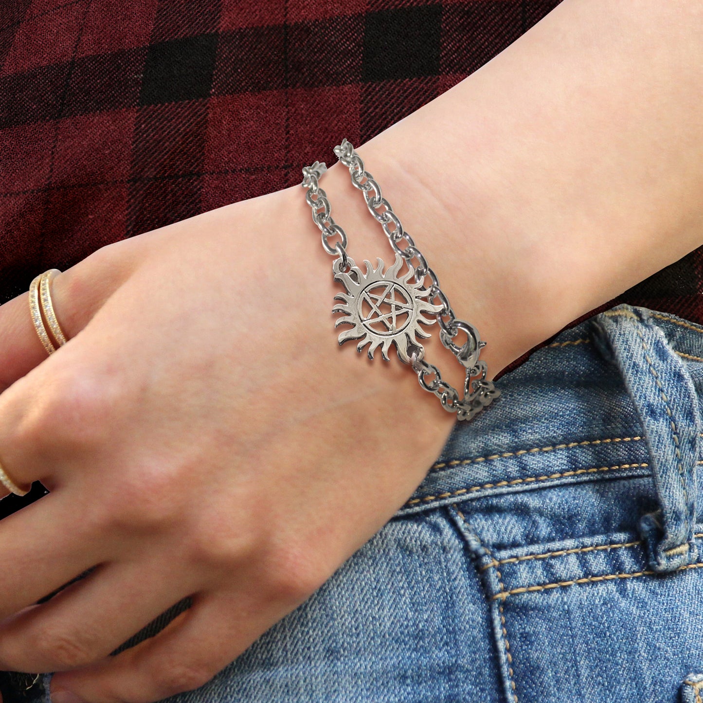 Close up of a model's wrist, wearing a silver bracelet. Attached to the bracelet is a charm in the shape of the anti-possession symbol.