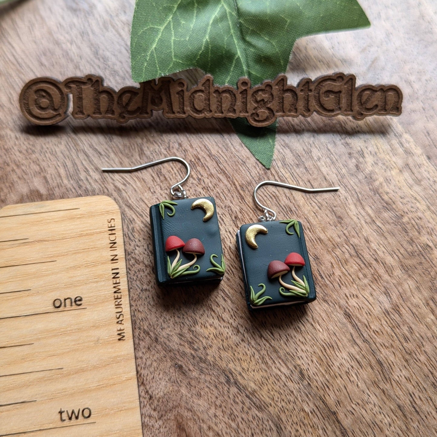 A pair of dangle earrings shaped like books, with tiny moons and mushrooms on the front.