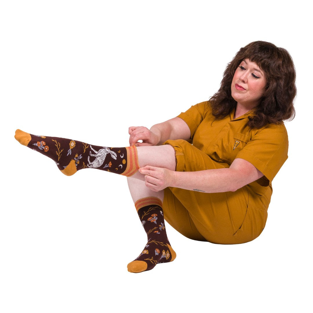 Woman wearing a mustard yellow dress and patterned socks sitting on the floor.
