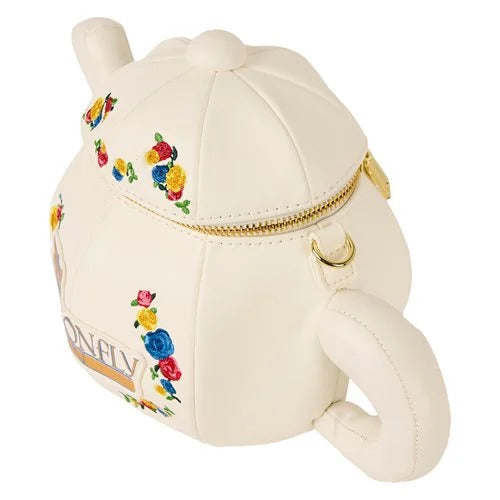 A white purse against a white background. The purse is shaped like a teapot. Around the front are colorful flowers. Gold and blue text says "Dragonfly Inn," with a gold and blue dragonfly next to it. The top of the teapot has a brass zipper.
