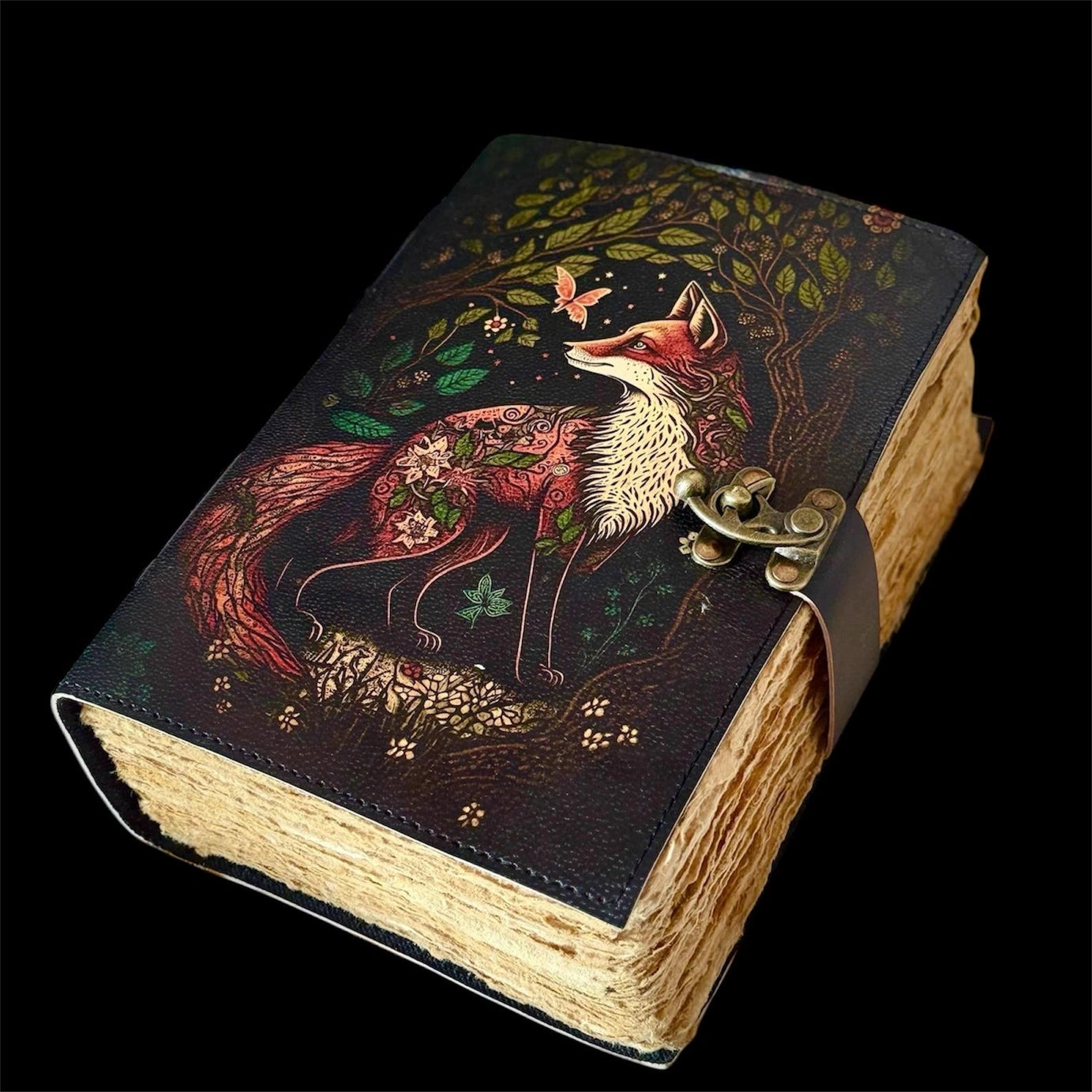 A leather journal against a black background. The cover depicts a red and white fox next to a dark forest.