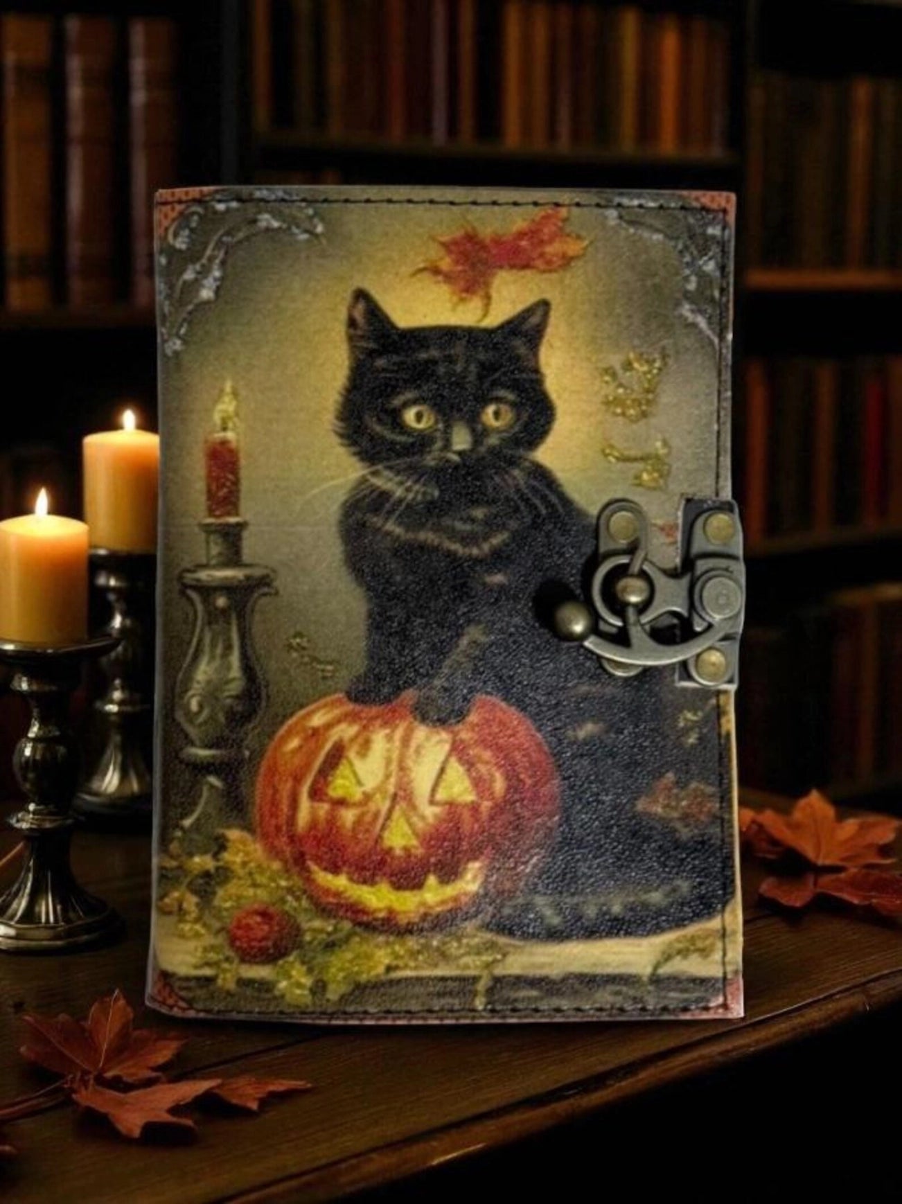 A leather journal on a wood table, next to lit candles. The cover depicts a black cat standing on a Jack-o-lantern. Behind the journal is a dimly lit bookcase.