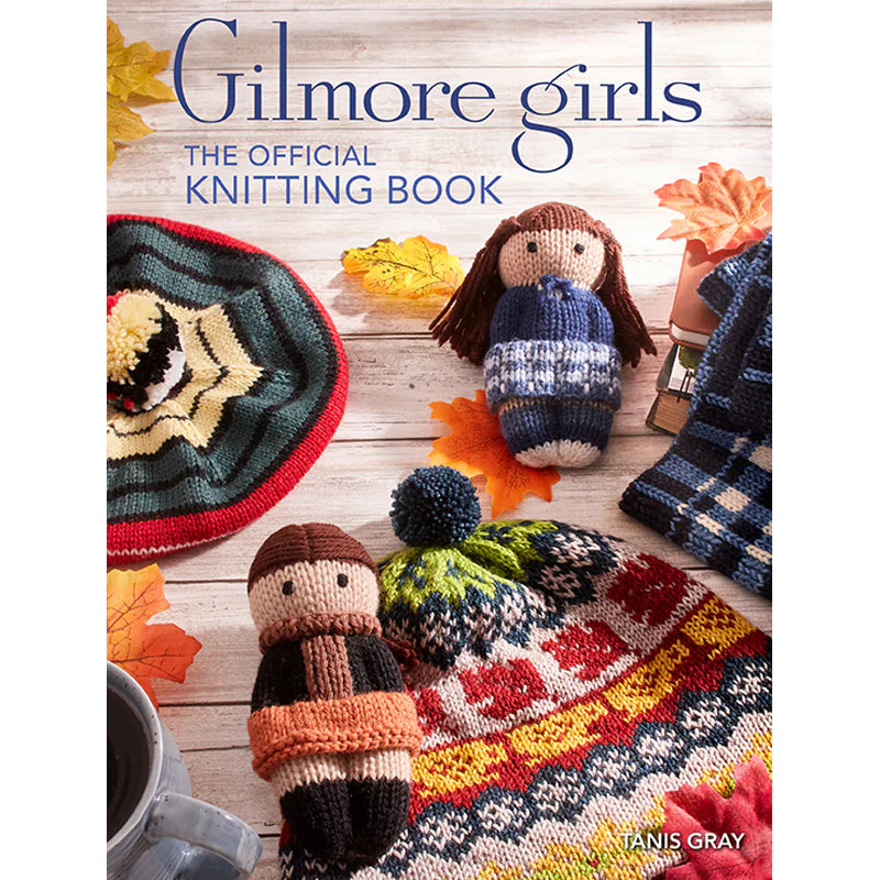 An image of a hardcover book cover against a white background. On the cover are knitted effigies of the main characters from the TV series The Gilmore Girls. Around them are other knitted items, including a hat with coffee mugs, a beret, and a blue plaid napkin. Blue text says "Gilmore Girls, the official knitting book." 