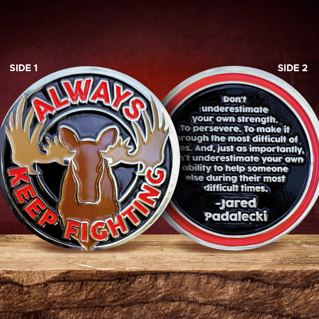 Two sides of a motivational coin with a moose design and inspirational quote on a wooden surface.