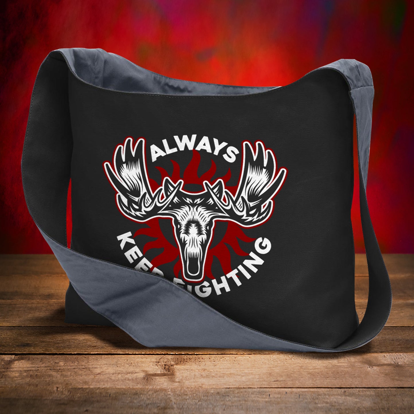 Black bag with moose graphic and 'Always Keep Fighting' text on a wooden surface with red background
