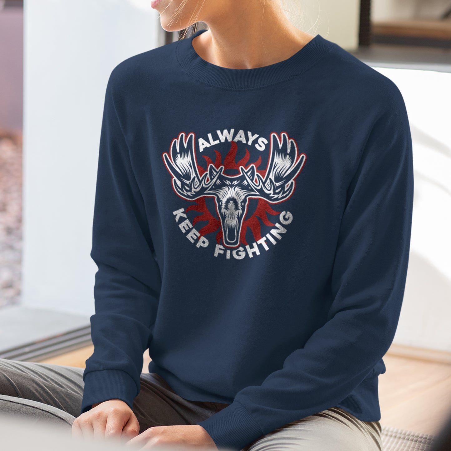 A model wearing a navy blue sweatshirt. On the front is a depiction of a moose head, with "always keep fighting" in white text.