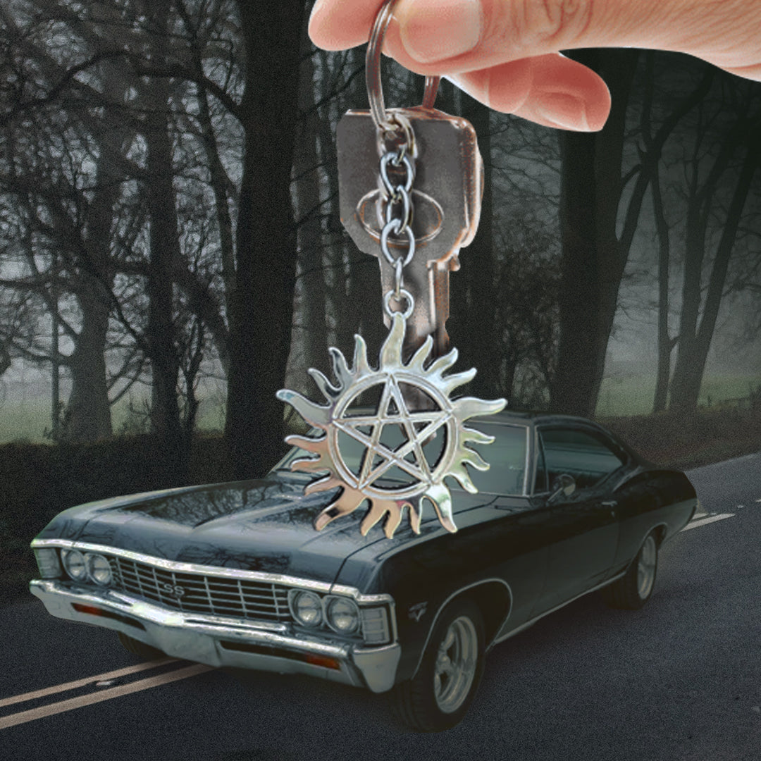 A model's hand holding an anti-possession symbol keychain. In the background is a black Chevy Impala on a dark road