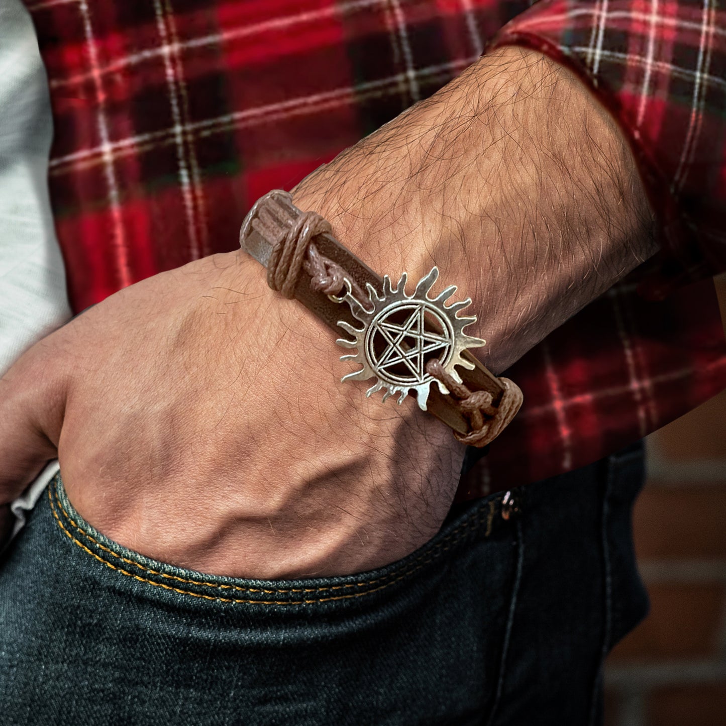 Close up of a model's wrist, wearing a brown leather bracelet with a silver charm at the top. The charm depicts the anti-possession symbol.