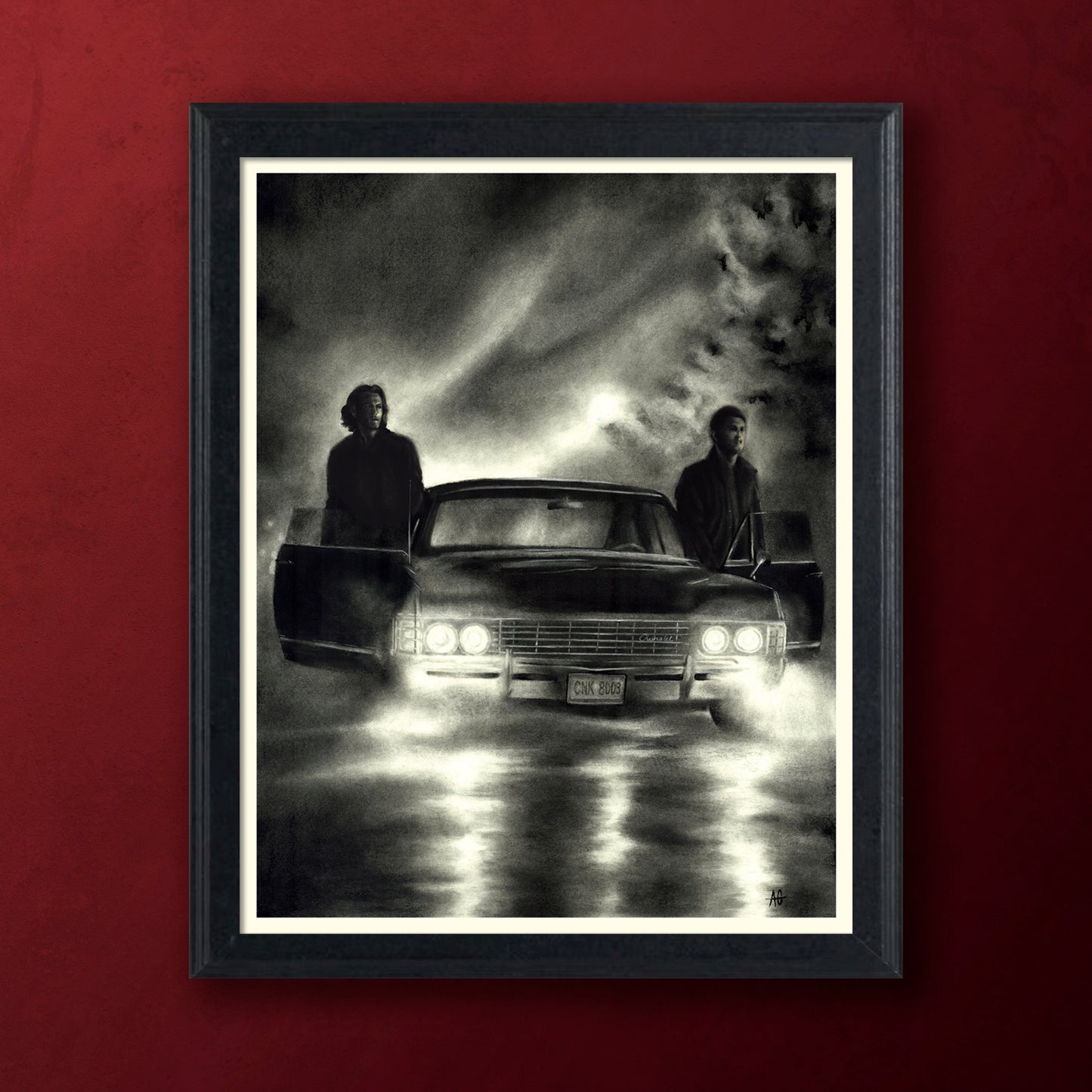 A framed black and white art print depicting a 1967 Impala with two brothers standing beside it under a dramatic cloudy sky, mounted against a solid dark red wall.