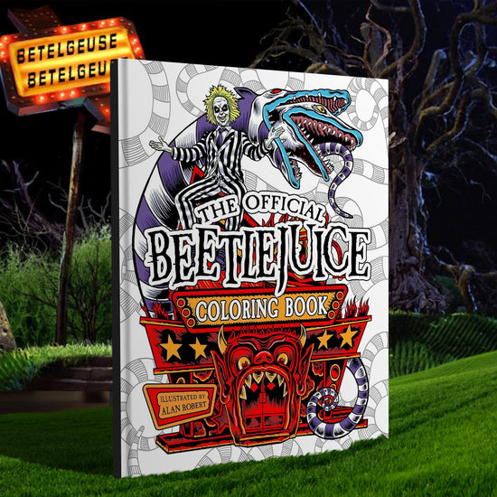 A white hardcover book on a green lawn, with a dark sky and spooky, dead trees in the background. On the cover are drawings of characters from the movie Beetlejuice, including the titular character and a purple and white stripped snake. At the bottom is a drawing of a funhouse with a devil's face over the door. Black and white text says "The official Beetlejuice coloring book"