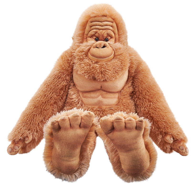 Close up view of a stuffed Bigfoot doll, against a white background. The doll has reddish hair, with a light brown wrinkled face and very large brown feet.
