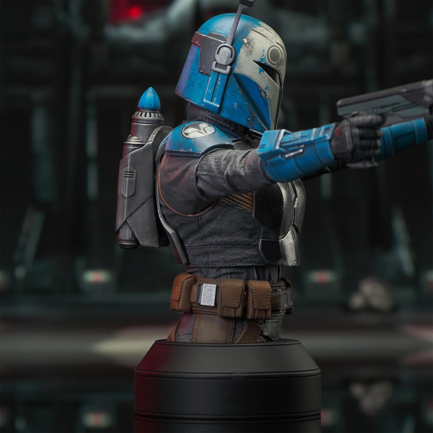 A resin bust depicting Bo-Katan Kryze in her Nite Owl armor, holding blasters in each outstretched hand. In the background is a hangar bay.
