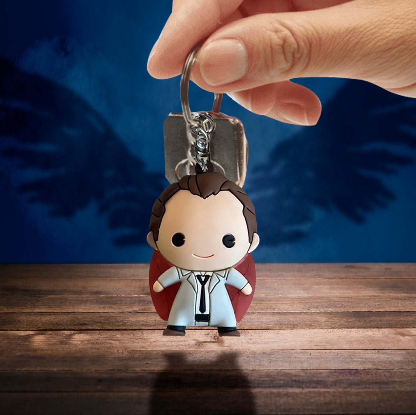 A model's hand holding a foam keychain depicting the angel Castiel with red wings