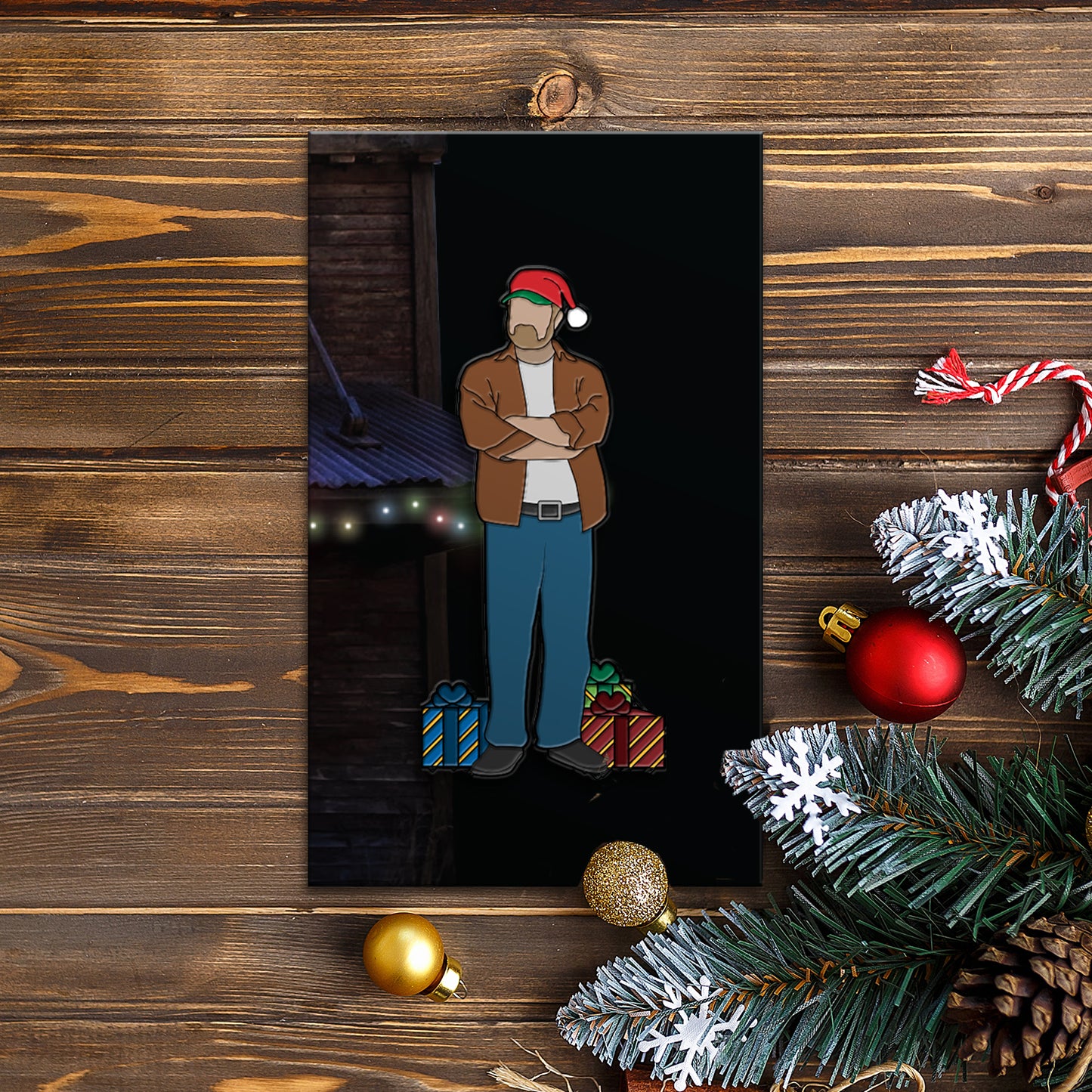 An enamel pin depicting Bobby Singers  in a  Santa hat, arms  crossed, standing next to  Christmas gifts