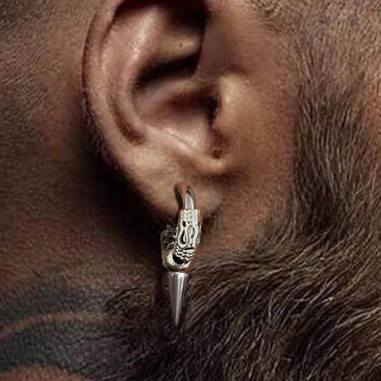 Close up of a model's ear wearing a silver earring. The earring is a hoop, with a cone-shaped pendant hanging from the bottom edge. At each side of the hoop are small textured cuffs, with a snake-shaped section at the center of each.