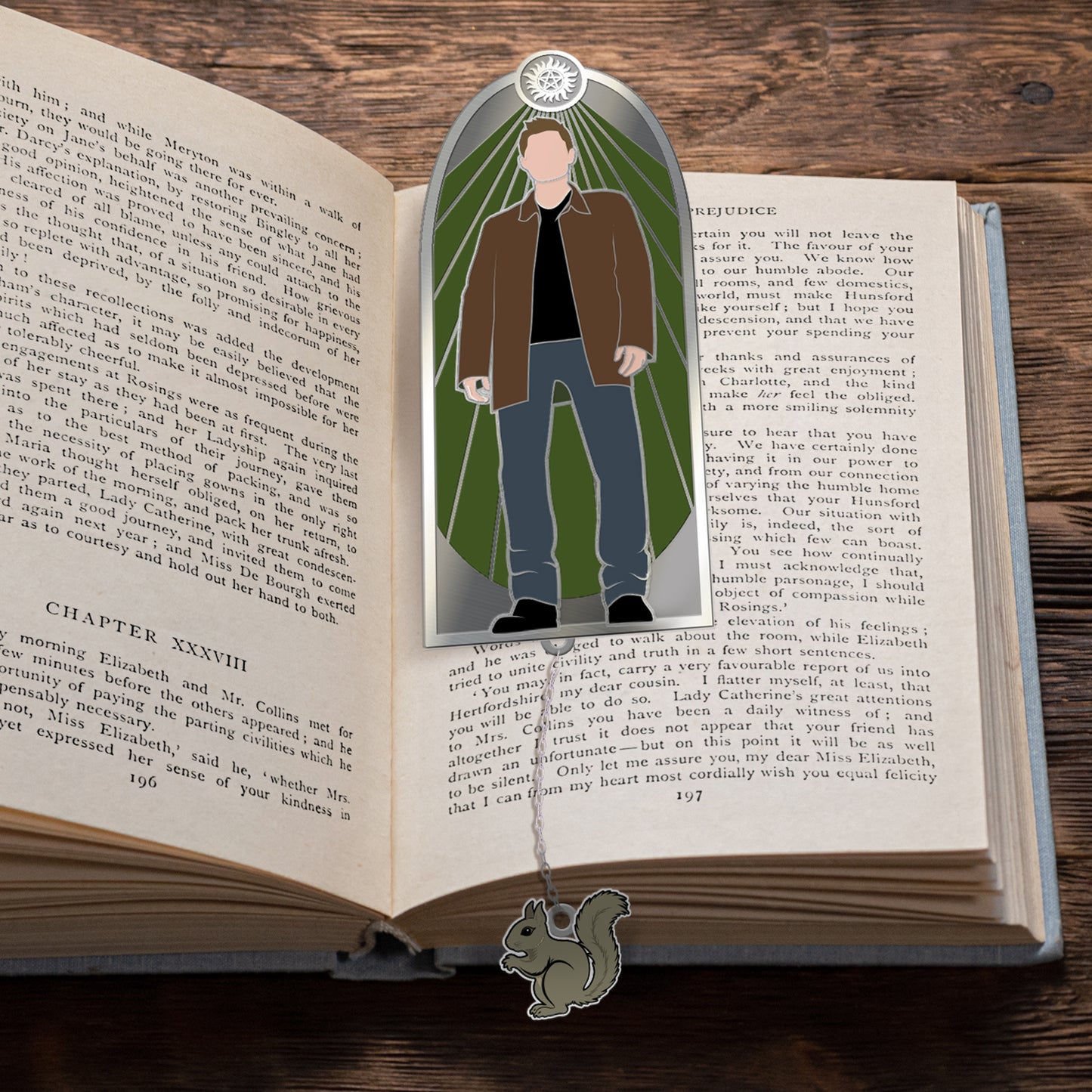 A bookmark on an open book. The bookmark depicts Dean Winchester against a green background. At the bottom of the bookmark is a Squirrel-shaped charm, attached to a chain.