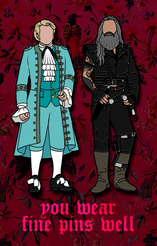 A pair of enamel pins on a red card. The left pin depicts a gentleman in light blue finery from the late 1600s. The right pin depicts a bearded man in dark pirate clothes. Red text at the bottom says "You wear fine things well." The background of the card has a pattern of birds and flowers.