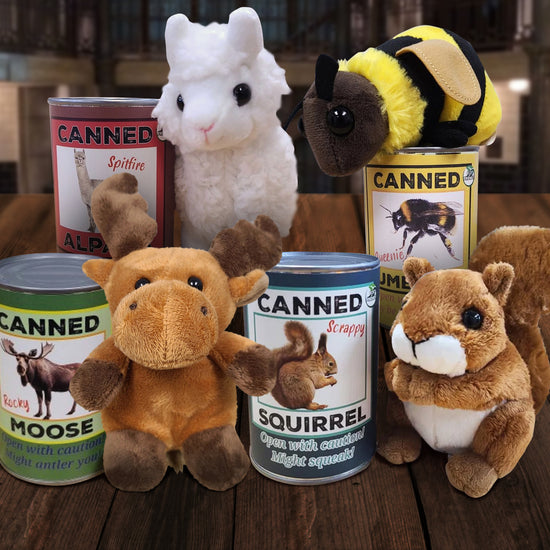 Four small plushies and tin cans on a wooden table. The four plushies are an alpaca, a bumblebee, a moose, and a squirrel, and each plushie has its own specific can.