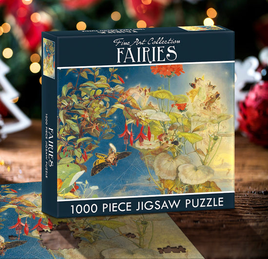 A puzzle box labeled "Fine Art Collection: Fairies - 1000 piece jigsaw puzzle". The preview depicts an illustrative, traditional-style design featuring several faeries on leaves, flowers, and moths in front of a blue sky. A map is under the box, and in the background is a lit Christmas tree.