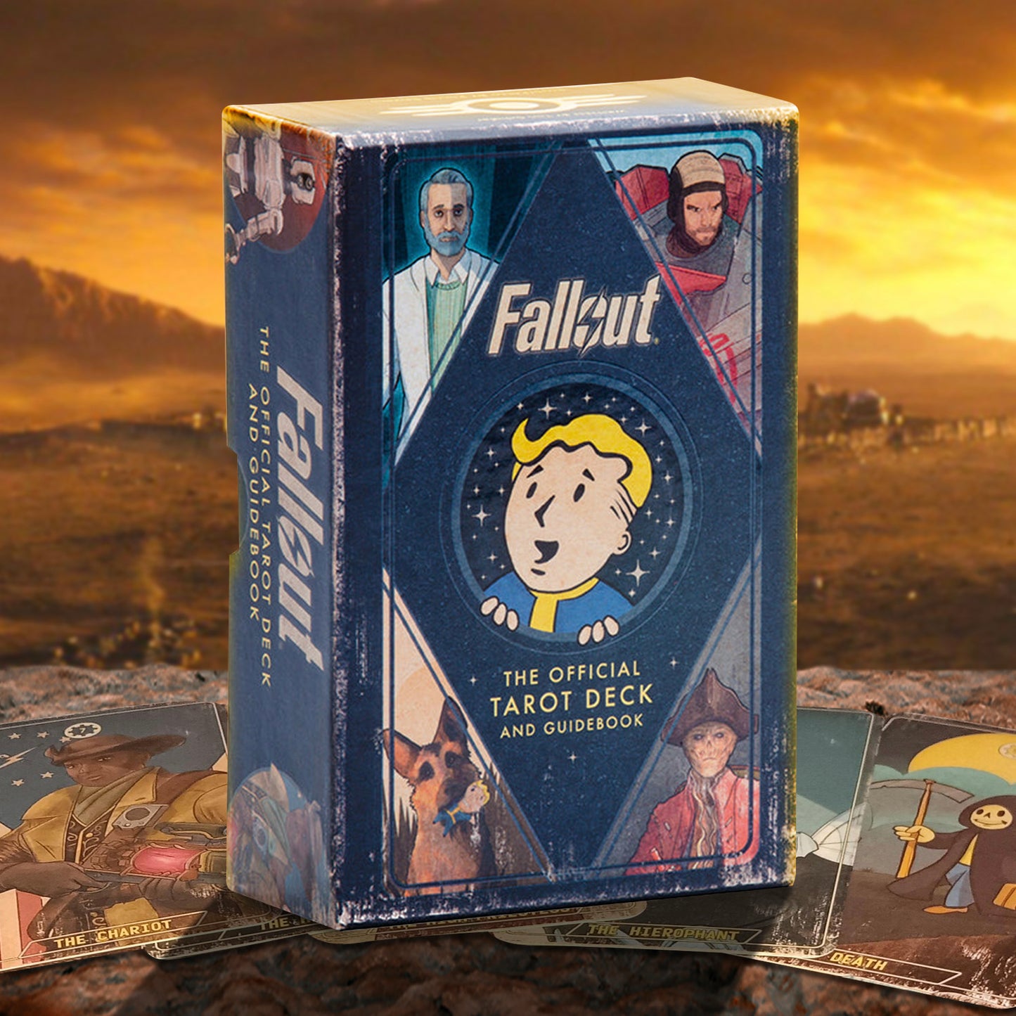 Fallout The Official Tarot Deck and Guidebook box standing upright, with several tarot cards spread around it on a rocky surface against a golden desert landscape background.