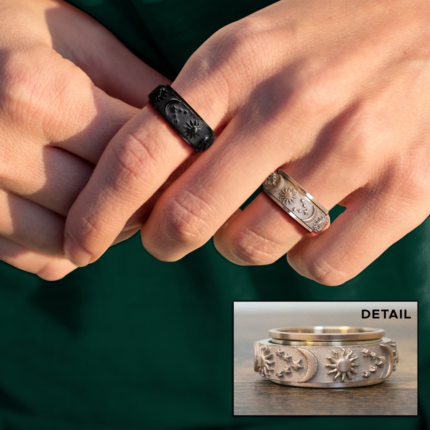 Close up of a model's hand, wearing two rings. One ring is black, the other is silver. Around the surface of the rings are raised depictions of the sun, the moon, and stars. Behind the model's hand is a dark greenbackground. At the bottom right corner is an inset image of the silver ring, showing a close up of the ring's details.