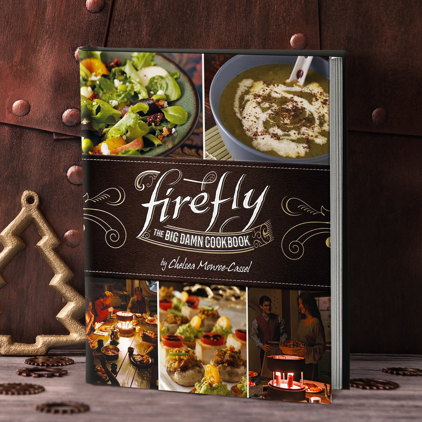 An upright cookbook. The cover features images of foods and characters from the TV series "Firefly." Across the middle is a brown banner with old fashioned filigree in white. Text in the center says "Firefly, the big damn cookbook."