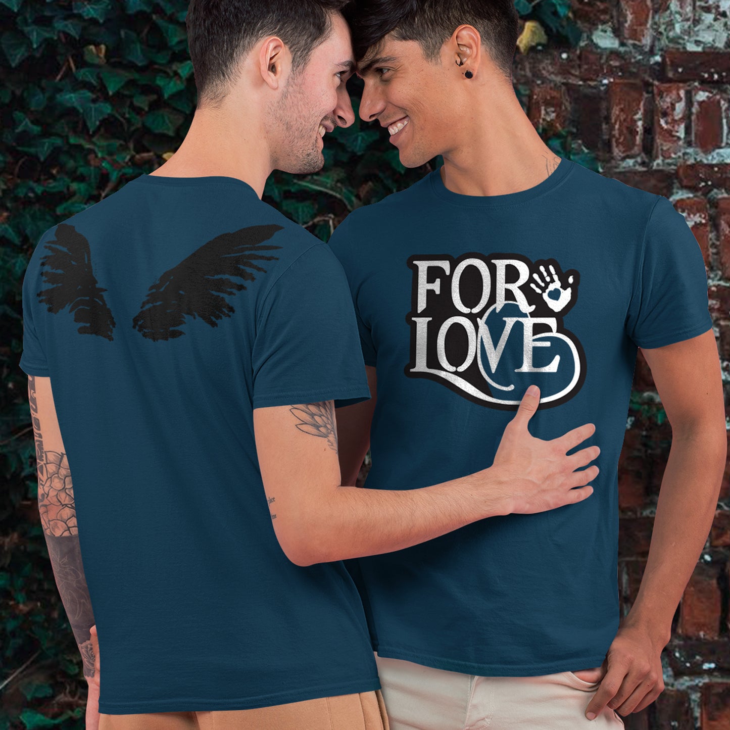 Two people wearing navy blue t-shirts with a design and text, standing close together against a brick wall.