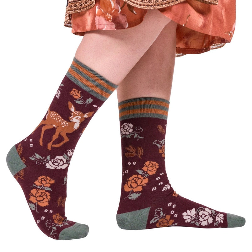 A model's feet wearing a pair of maroon socks. The socks feature a pattern of orange and white flowers, with a brown fawn on the side.
