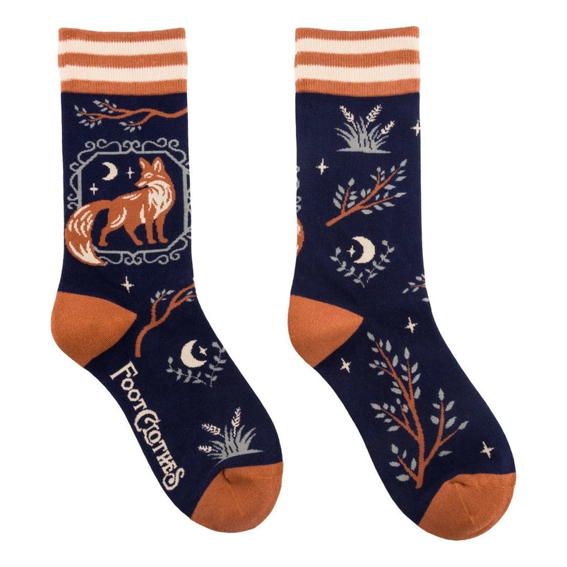 A pair of crew length black socks. The socks feature a pattern of tree branches and crescent moons, with a brown fox on the side.
