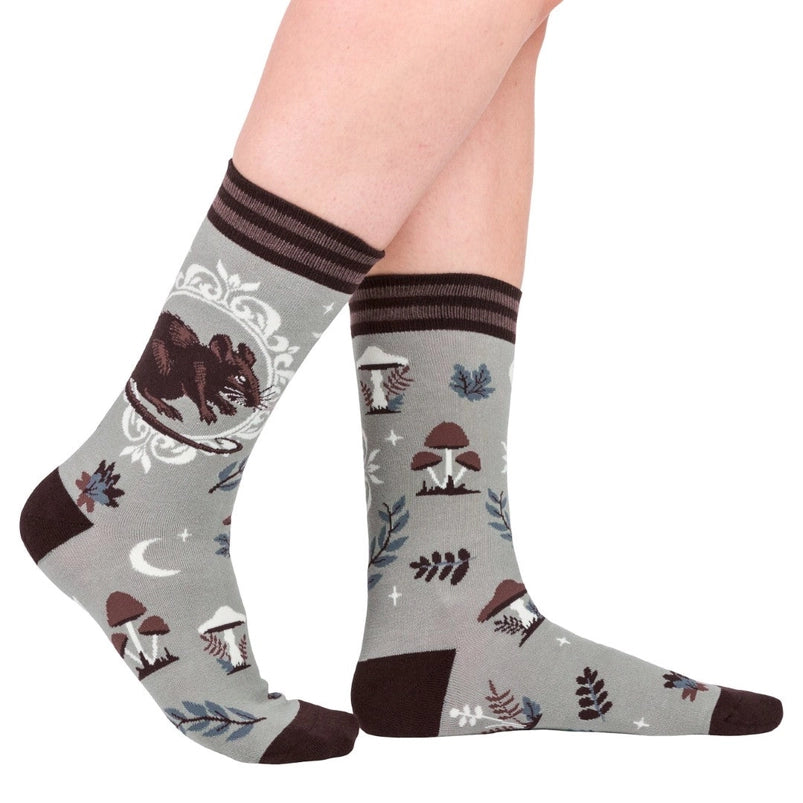 A model's feet wearing a pair of grey socks. The socks feature a pattern of brown and white mushrooms, with a brown rat on the side.