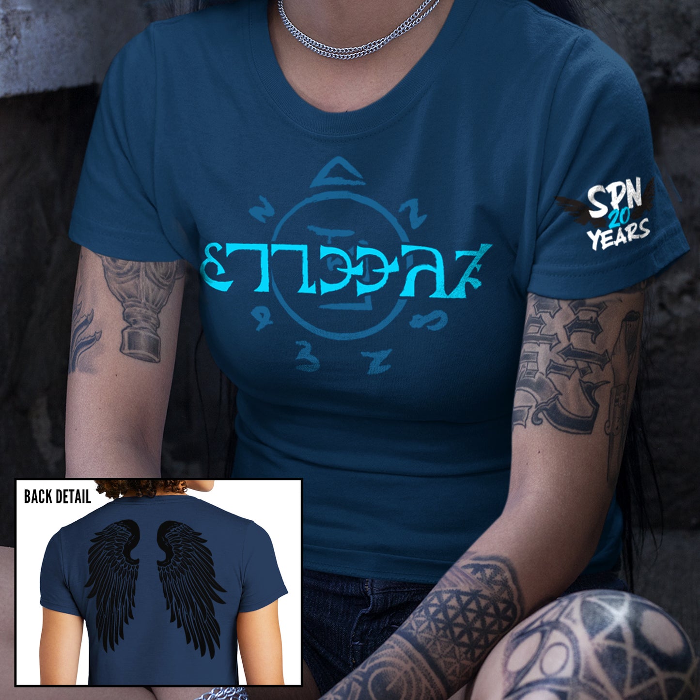 Two images of models wearing a blue t-shirt. The front of the shirt has light blue runes, which spell out the word "funnier" in the angelic language Enochian. On the left sleeve is a pair of black wings with white and blue text that says "SPN 20 years." The back of the shirt has a pair of large black angel wings.