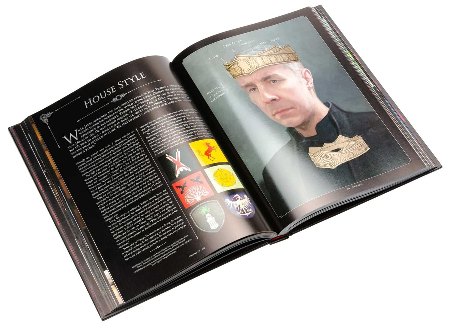 A two-page spread from the book. The pages depict a character from the series wearing a black robe and a gold crown. Text on the left page describes the house styles.