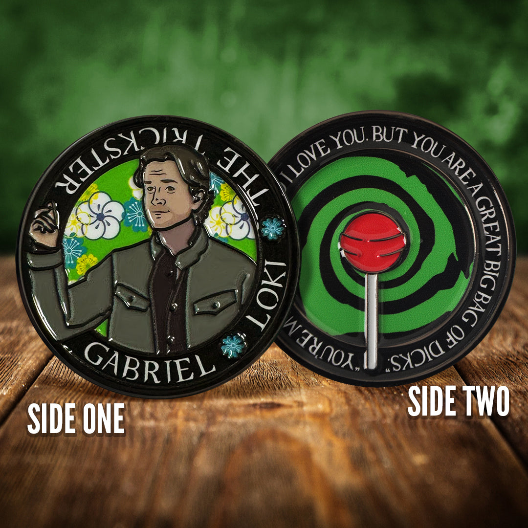 Front and back images of a challenge coin, side by side, on a wood table. The front depicts a drawing of Gabriel, the Trickster. Behind him are flowers on a green background. The back of the coin depicts a green and black swirl with a red lollipop in front of it. White text around the edge says "You're my brother. And I love you. But you are a great big bag of dicks."