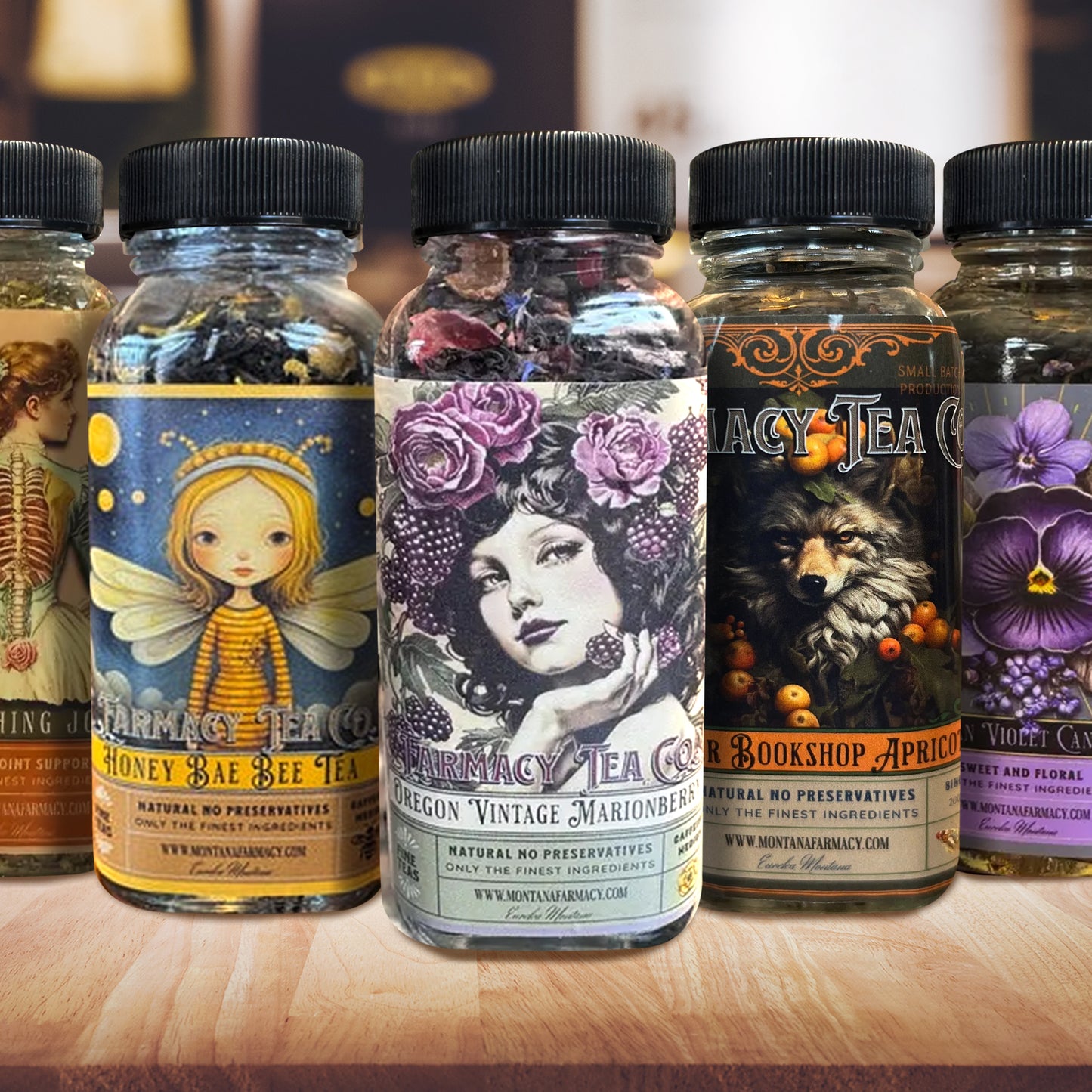 A row of glass tea jars with black lids on a wooden surface, featuring colorful vintage-style labels for flavors including Honey Bee, Oregon Vintage Marionette, Bookshop Apprentice, and Purple Clover.
