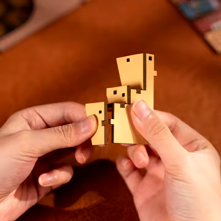 A close-up picture of two hands snapping together 2 small wooden pieces of the book nook kit.