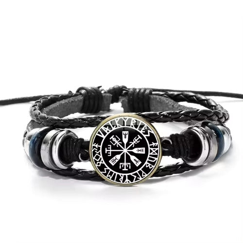 Close up of a black braided bracelet on a white background. At the center is a black and silver round charm depicting Nordic runes in the shape of a compass.