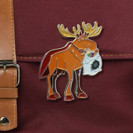 A closeup on a red bag with metal buckle. There is a large pin of a moose in a devil costume carrying a sack full of candy with an anti-possession symbol on it.