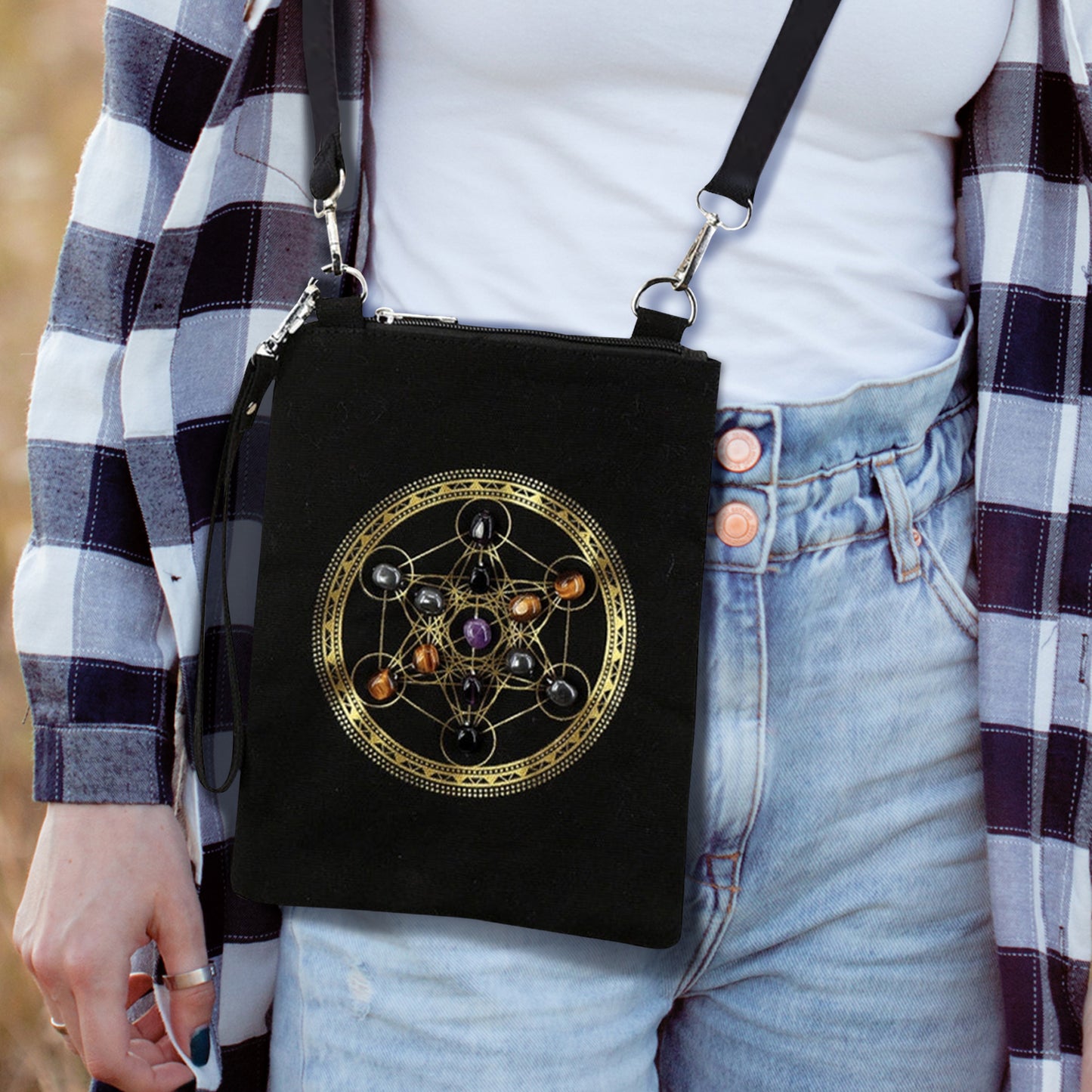 A small black crossbody bag on a female model. On the front of the bag is the Heaven's Portal symbol in gold ink, with gemstones inset in the circles. The bag has a small wrist strap attached at one side, and a larger shoulder strap at the top.