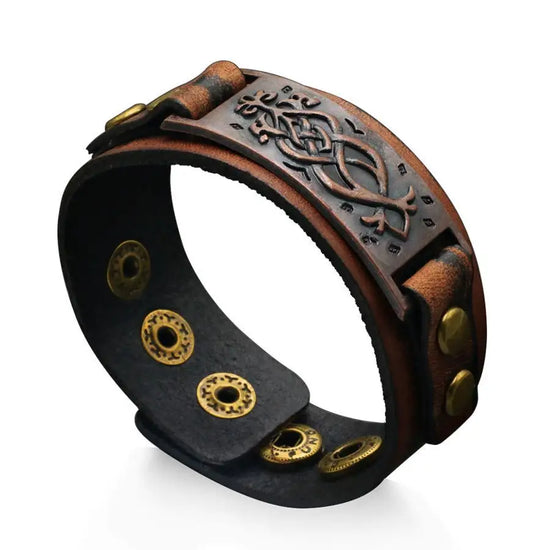 A dark brown leather cuff bracelet inspired by Viking imagery/style. It has brassy metal details, an adjustable button closure, and a brown metal plate with visual detailing.