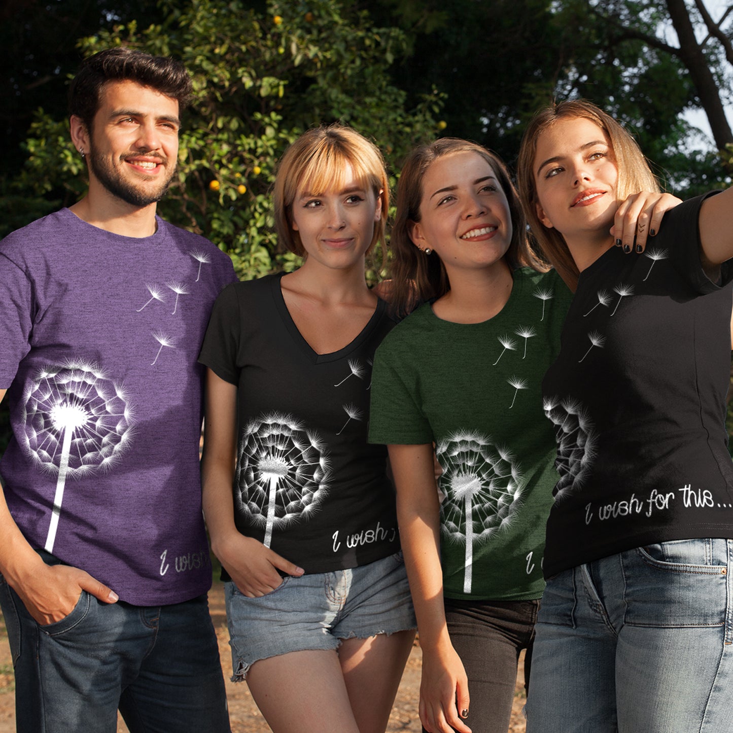 Four models side by side, standing in front of trees. Each model is wearing a T-shirt with a drawing of a white dandelion and seeds on the front. One shirt is purple, one is dark green, and two are black. At the bottom of each shirt is white scripted text that says I wish for this.