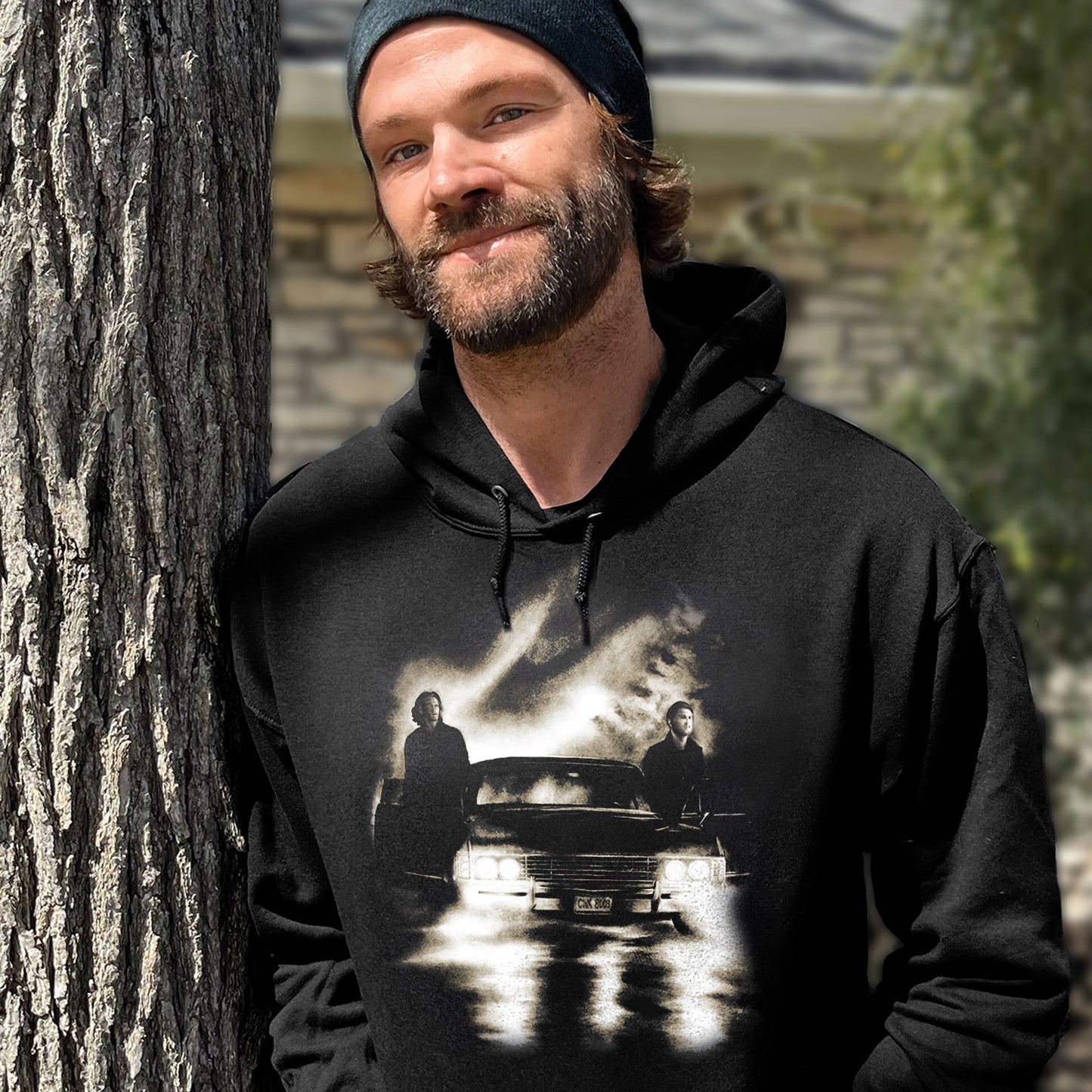 An image of Jared Padalecki in a black hoodie. On the front is a drawing of Sam and Dean Winchester with Baby