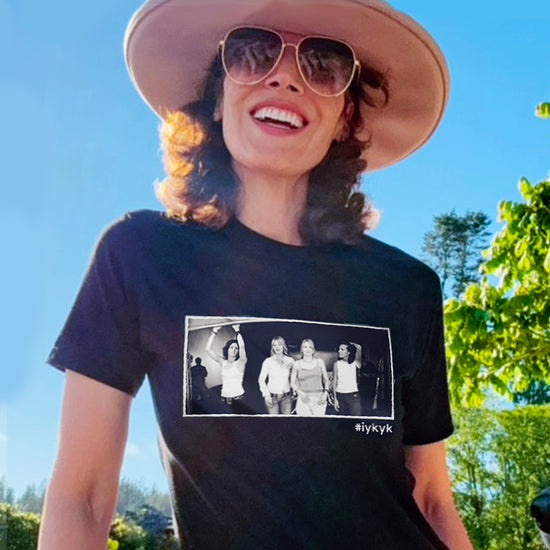 An image of actress Jennifer Beals wearing a black t-shirt. A female model wearing a black T-shirt, under a blue sky. On the front is a black and white image of characters from the TV series "The L Word." Under the image is the hashtag #ifkyk