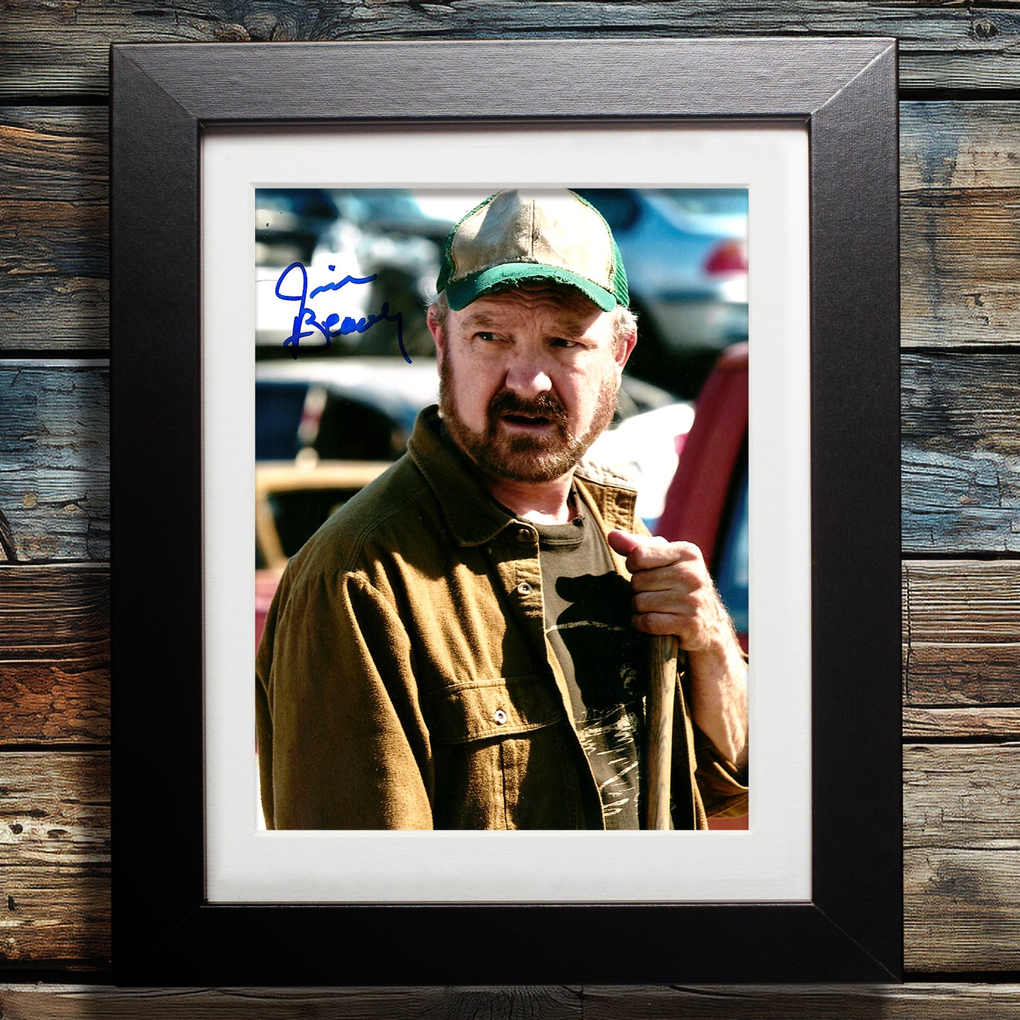 A black framed photograph against a dark wood-plank wall. The photograph depicts actor Jim Beaver in costume as Bobby Singer. In the top left corner is Jim's autograph in blue ink.